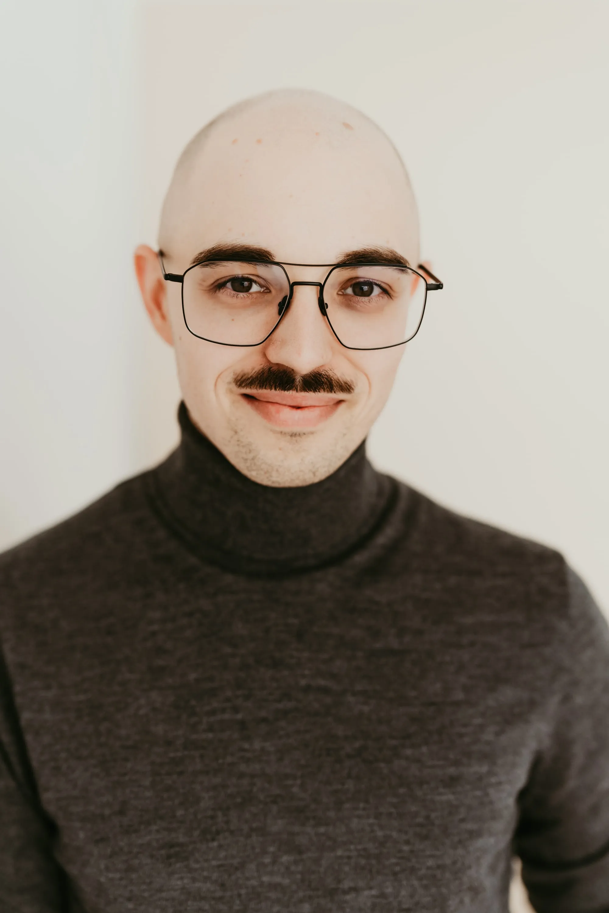 Benjamin Goecke, wearing glasses and a dark grey turtleneck, looking at the camera.
